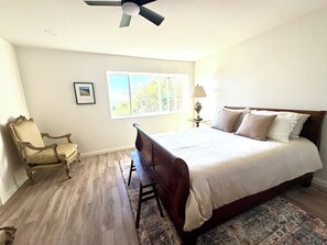 A bedroom with a bed, a chair, a lamp, a window, and a ceiling fan. - 5 minutes to the beach! The Hideaway on Lillie Ave. (Summerland)
