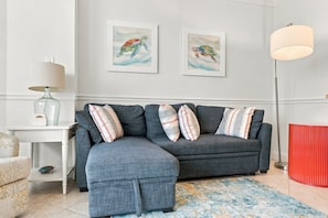 A modern living room with a grey sectional sofa, two framed artworks, a floor lamp, and a patterned rug. - Tideview Retreat with Indoor and Outdoor Pools (Myrtle Beach)