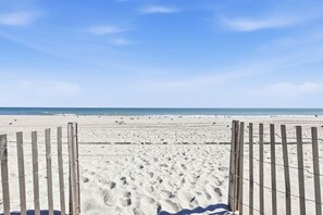 Uma praia arenosa com uma cerca de madeira em primeiro plano e um céu azul límpido.
