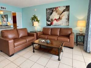 A living room with two brown leather sofas, a wooden coffee table, a painting on the wall, and a lamp on a side table. - PCB Beach Escape, King, Bunks + 2 Full Baths, Summit Resort (Panama City Beach)