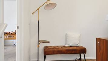 Une pièce avec un banc marron, une lampe sur pied, une petite table et un coussin blanc.