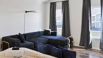 A modern living room with a sectional sofa, a floor lamp, and large windows with curtains.