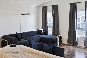 Ein modernes Wohnzimmer mit einem Ecksofa, einer Stehlampe und großen Fenstern mit Vorhängen.