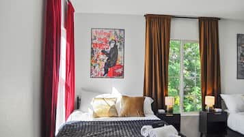 Une chambre d’hôtel avec un lit, deux tables de chevet, une fenêtre avec des rideaux et un tableau au mur.