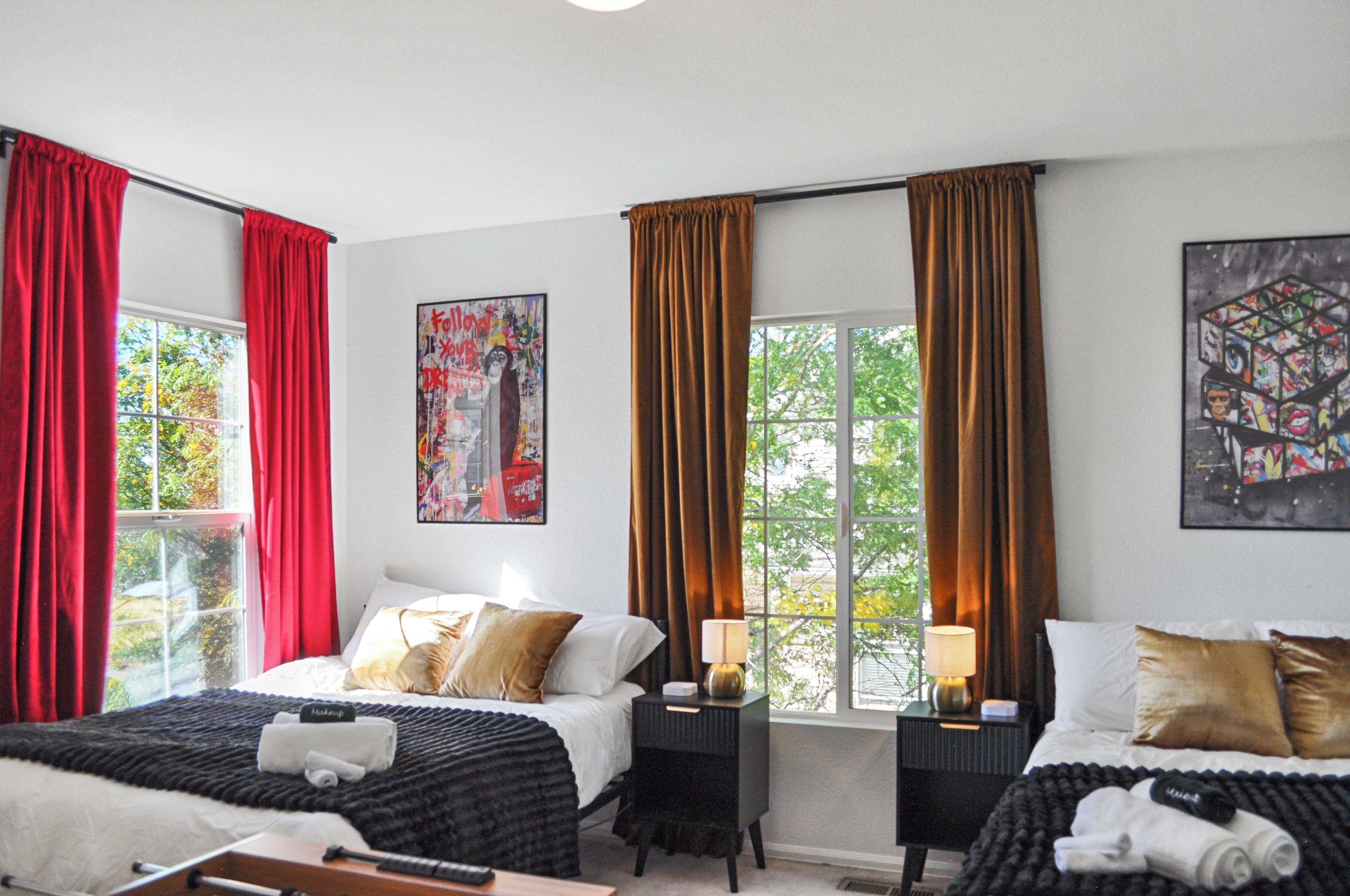 Une chambre d’hôtel avec deux lits, des rideaux rouges et bruns, et des œuvres d’art accrochées aux murs.