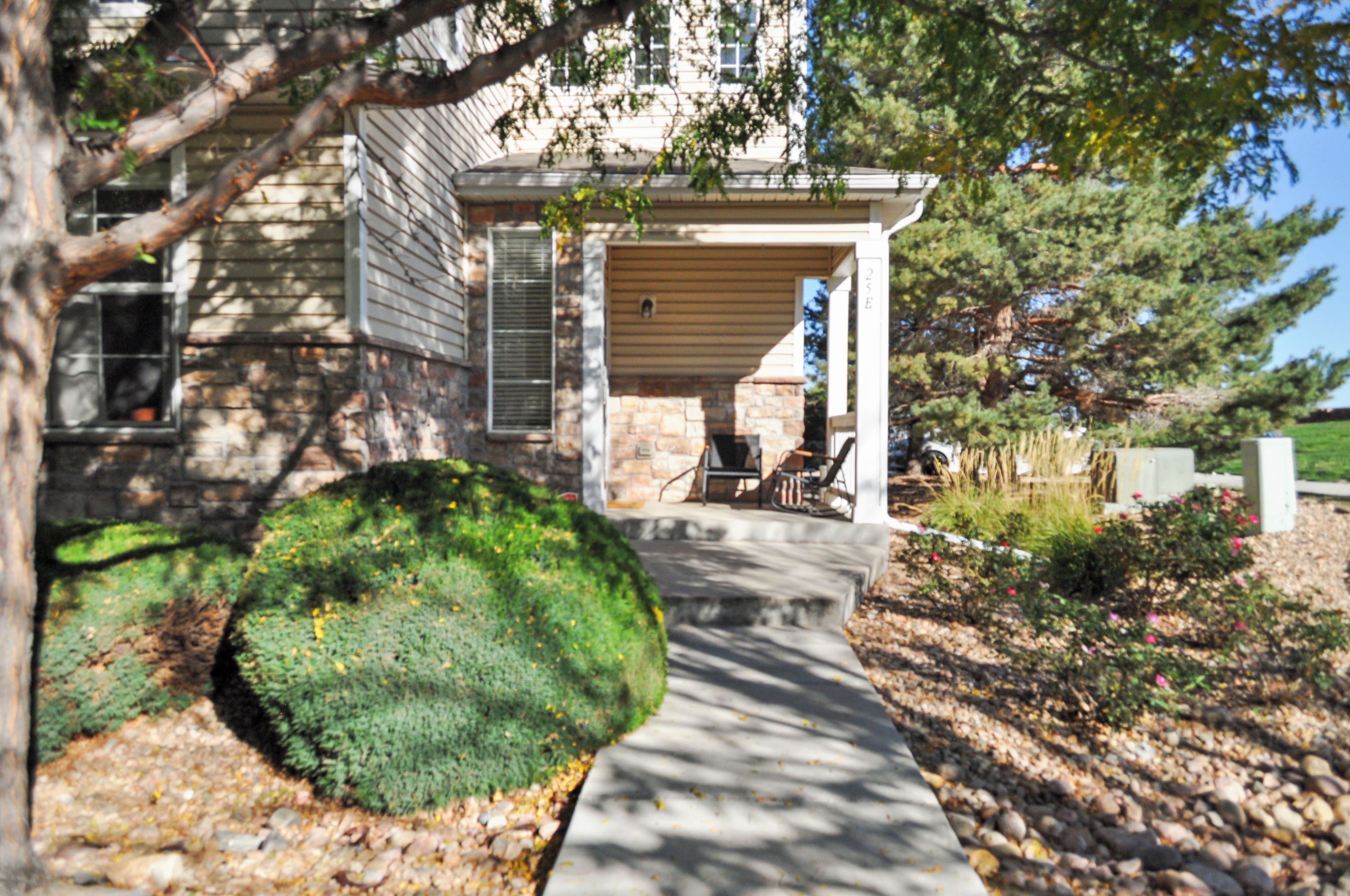 A house with a stone facade, a covered porch, and a well-maintained garden with a large bush and a pathway leading to the entrance.