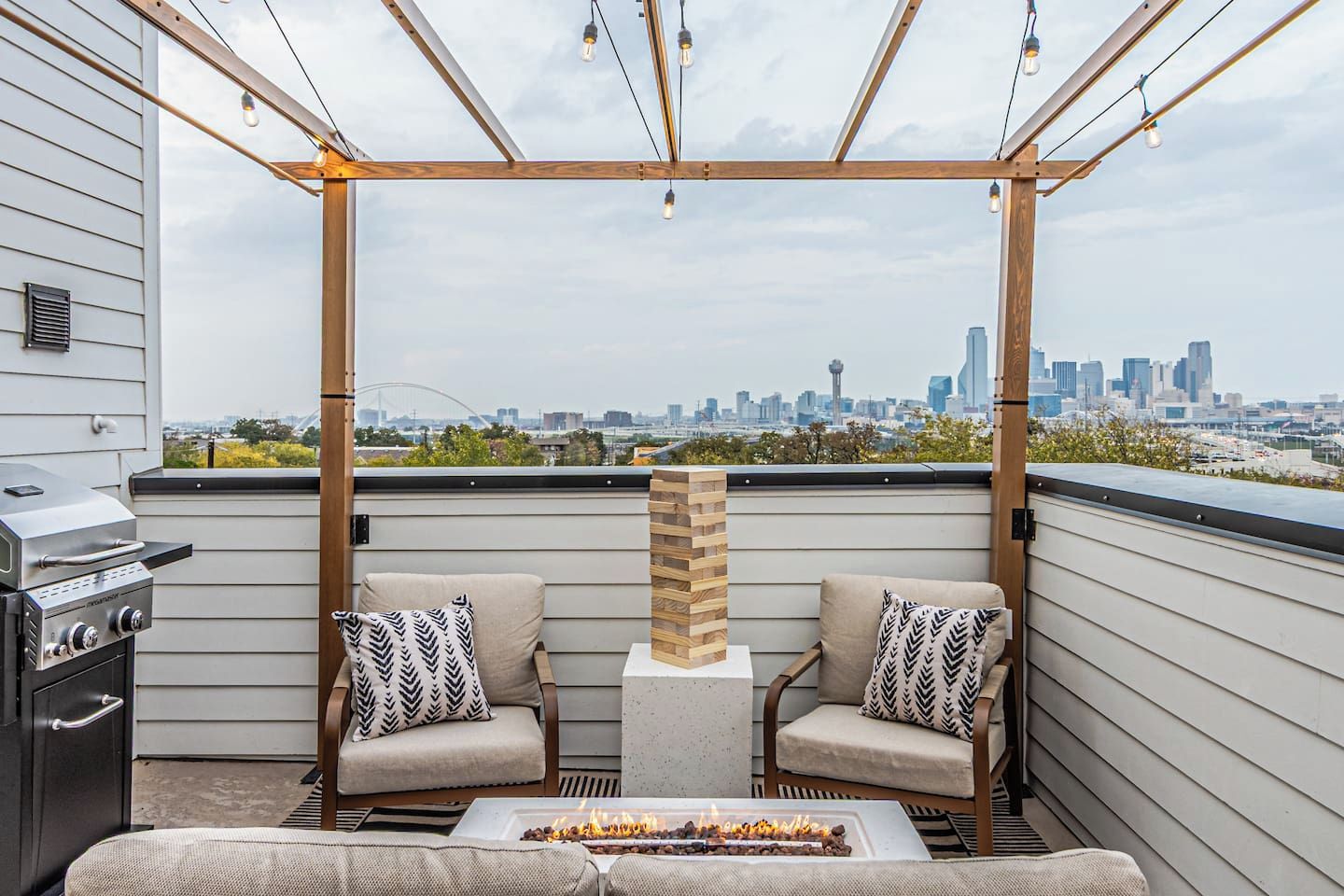 A rooftop patio with two cushioned chairs, a grill, and a fire feature.