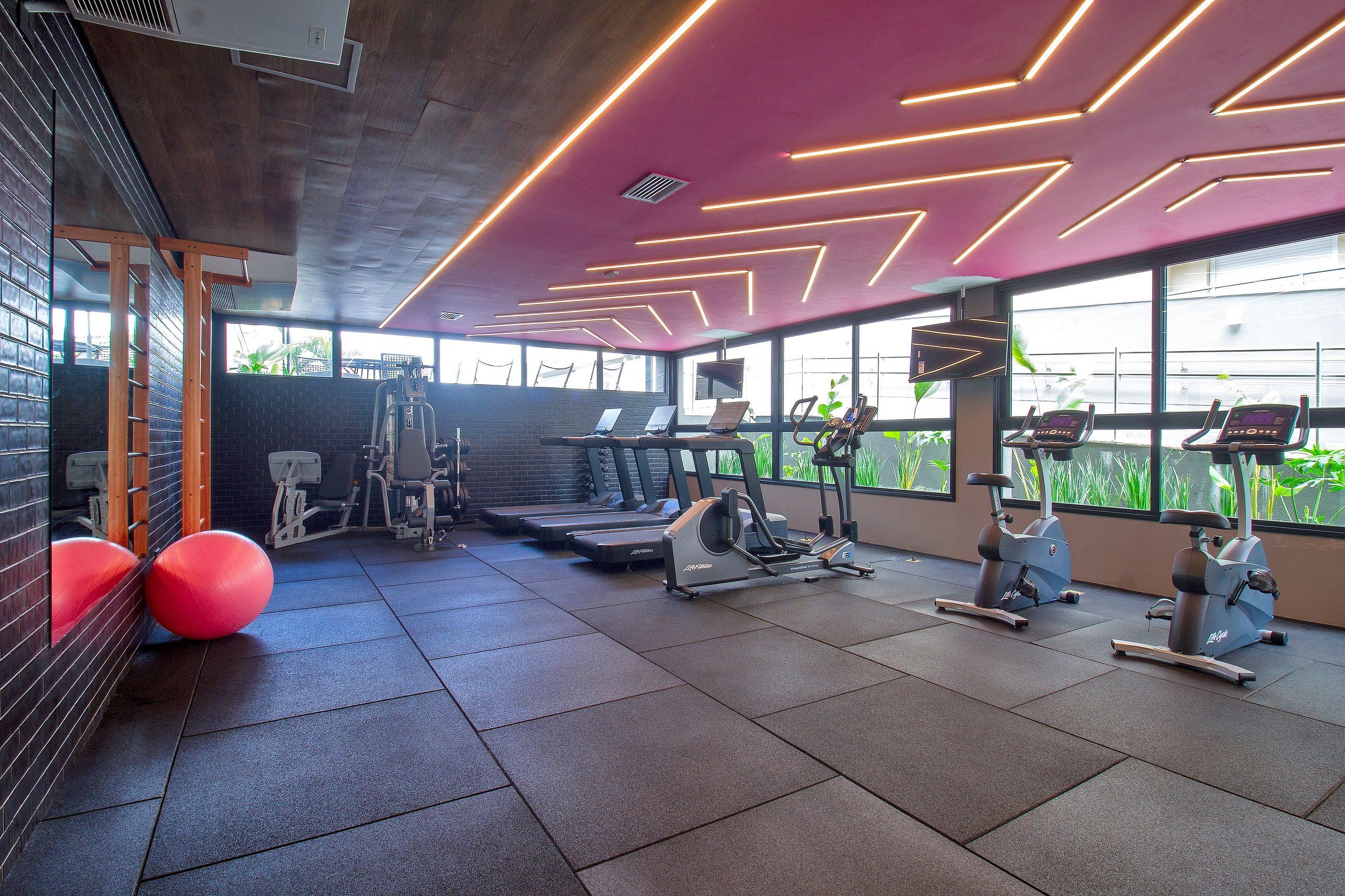 Un gimnasio con equipo de ejercicio, ventanas amplias y un diseño de techo rojo.