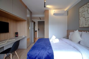 Habitación de hotel con cama, escritorio, silla, televisor y baño visible a través de una puerta abierta.