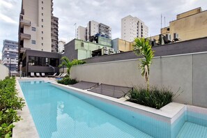 A swimming pool with lounge chairs and a small palm tree, surrounded by high-rise buildings.