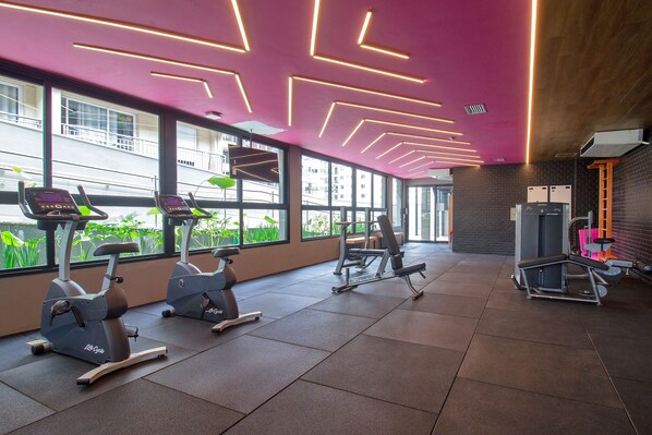 Un gimnasio con equipo de ejercicio, amplias ventanas y un diseño moderno en el techo.