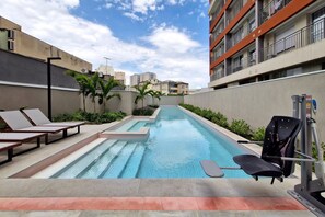 Una piscina con sillas de descanso y un kayak, rodeada de edificios.