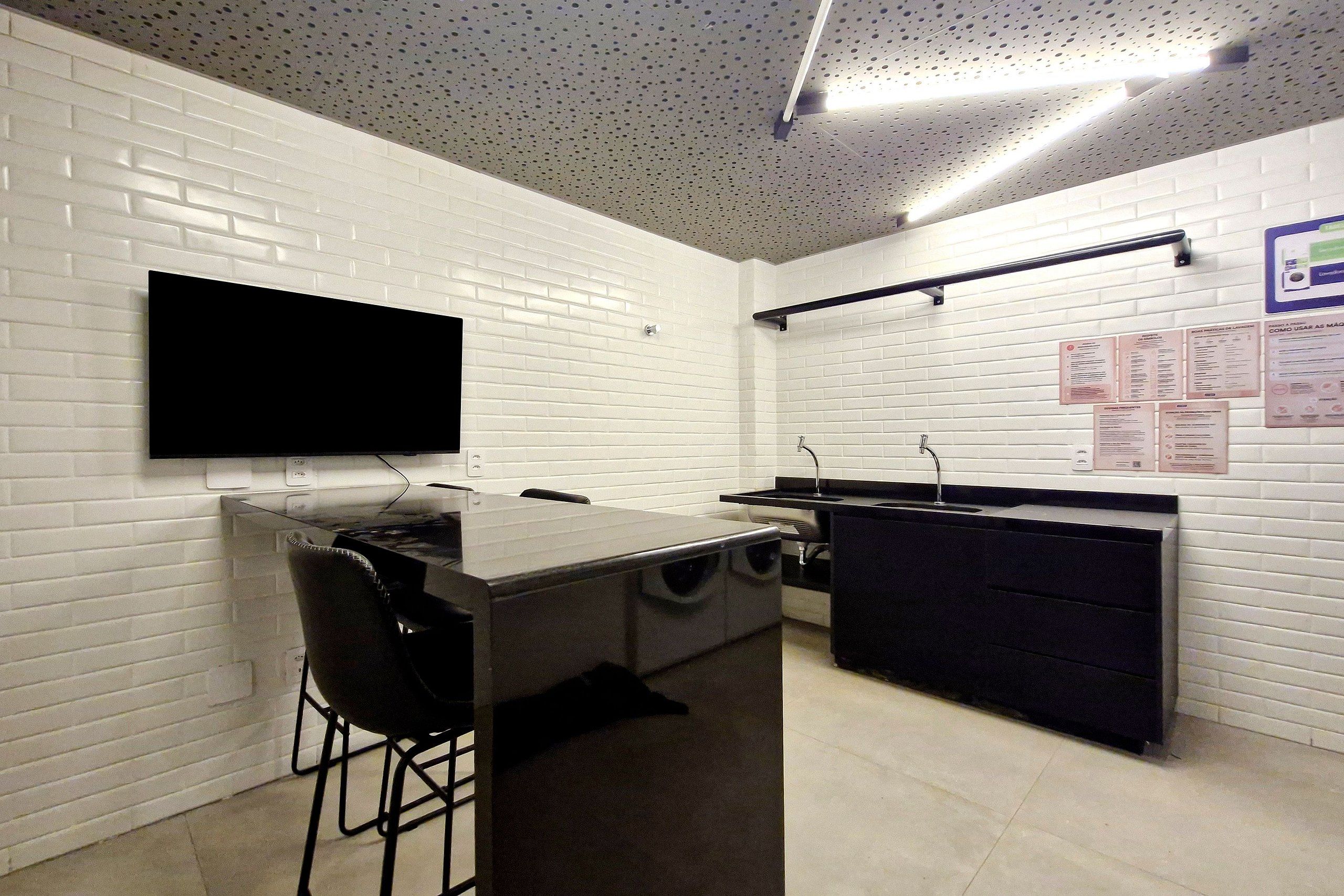 Una cocina moderna con paredes de ladrillo blanco, un televisor de pantalla plana sobre la encimera y una barra con taburetes.