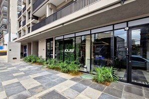 A modern building with a glass storefront, outdoor seating, and a checkered tile pavement.