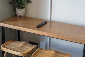 Una mesa de madera con un control remoto, dos sillas de madera y una planta en maceta.