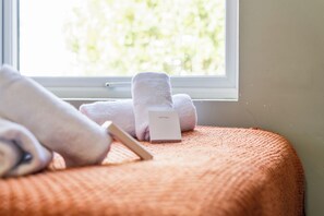 Ein Bett mit einem weißen Kopfkissen, einem weißen Handtuch und einer weißen Box mit dem Aufdruck 'SLEEPWELL' auf einer orangefarbenen, strukturierten Bettdecke.