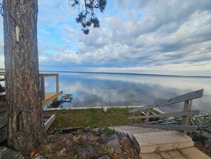 A wooden deck with a bench, a tree, and a view of a calm body of water.