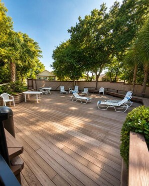 Une terrasse en bois avec des chaises longues et une table, entourée d’arbres.