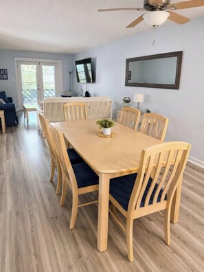 Ein Essbereich mit einem Holztisch, Stühlen, einem Deckenventilator und einem Fernseher an der Wand.