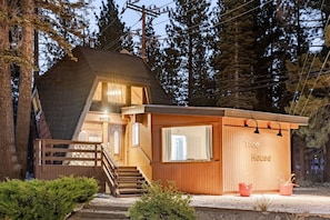 A wooden cabin with a staircase leading to a loft bedroom, a small porch area, and a visible number '1102'. - `Treehouse` 2 Bd Cozy Unique Home Steps to Village (Mammoth Lakes)