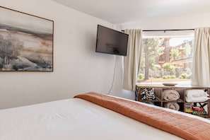 Une chambre d’hôtel comprenant un lit, un téléviseur à écran plat fixé au mur, une fenêtre avec des rideaux et une petite table avec des serviettes et des articles de toilette.