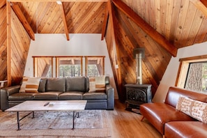 A cozy loft bedroom with a sloped ceiling, a sofa, a coffee table, and a wood-burning stove. - `Treehouse` 2 Bd Cozy Unique Home Steps to Village (Mammoth Lakes)