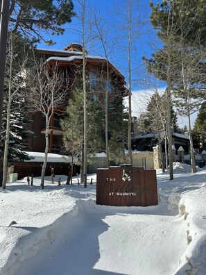 Une enseigne indiquant « The Village at Mammoth », avec un paysage enneigé et des arbres couverts de neige.