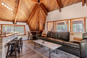 A cozy loft-style living area with a stone fireplace, leather sofa, and a dining area with stools. - `Treehouse` 2 Bd Cozy Unique Home Steps to Village (Mammoth Lakes)
