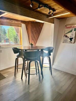 A dining area with a round table and four chairs, a wooden ceiling, and a poster on the wall. - Treehouse • Across from the Village. Walkable to Gondola & Ski‑Back Trail. (Mammoth Lakes)