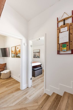 A hallway leading to a bedroom with a bed, a wooden bench, and a mounted artwork. - Treehouse • Across from the Village. Walkable to Gondola & Ski‑Back Trail. (Mammoth Lakes)