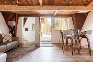 A cozy interior with a wooden ceiling, a sofa, a dining table with chairs, and a view through a door. - Treehouse • Across from the Village. Walkable to Gondola & Ski‑Back Trail. (Mammoth Lakes)
