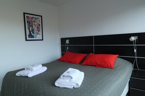 Ein Hotelzimmer mit einem Bett, zwei roten Kissen, einem gerahmten Kunstwerk an der Wand und zwei zusammengerollten Handtüchern auf dem Bett.