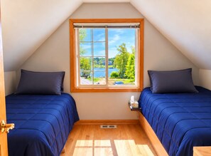 A room with two beds, a window with a view of greenery and a body of water, and a wooden floor. - Lakefront Getaway • Plenty of Car & RV Parking (Edgerton)