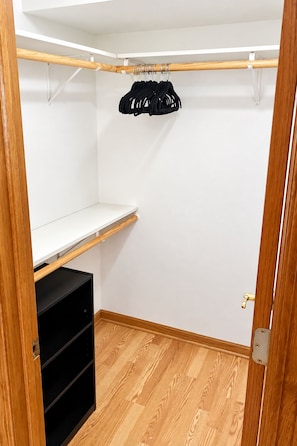 A walk-in closet with a wooden floor, a black shelving unit, and a clothing rack with hangers. - Lakehouse Getaway Plenty of Parking (Edgerton)