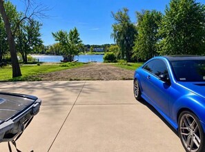 Une voiture bleue est garée sur une allée, avec un lac et des arbres en arrière-plan.