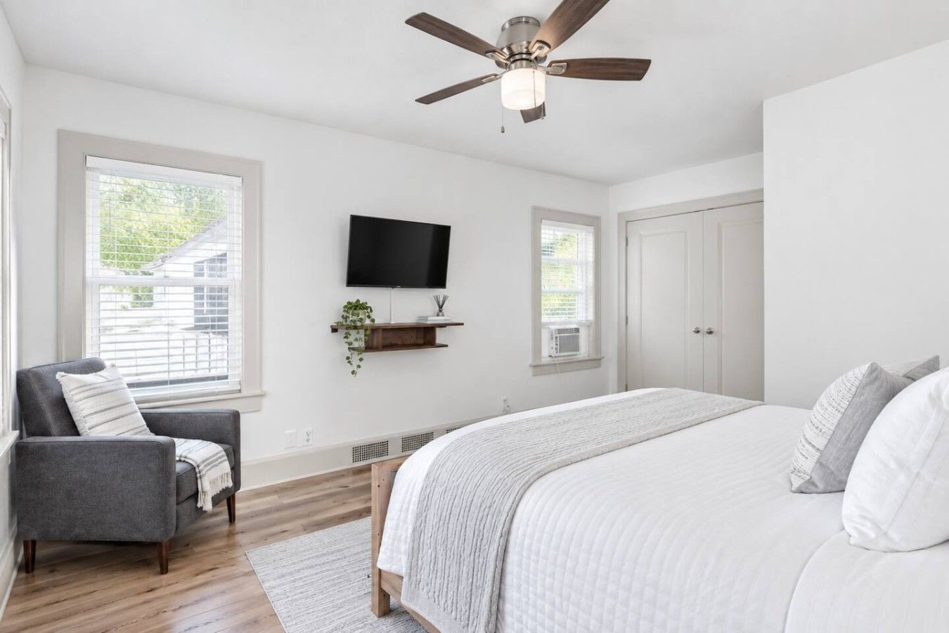 A bedroom with a bed, a chair, a TV, and a ceiling fan.