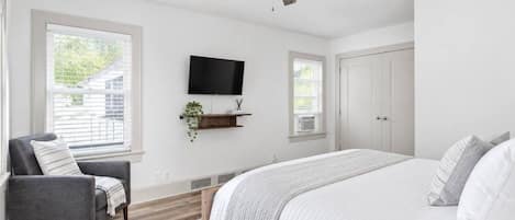 A bedroom with a bed, a chair, a TV, and a ceiling fan.