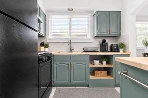 A kitchen with teal cabinetry, a black refrigerator, a built-in oven, a sink, and a window with blinds. - 714 Rockford apartment (Rockford)