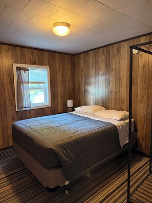 A room with a bed, a window with curtains, a bedside lamp, and a ceiling light fixture. - Cabin 3  • 2 BR 1 BA Cabin • Sleeps 5 • Lake Roland Frontage & Trail 3 Access (Toivola)