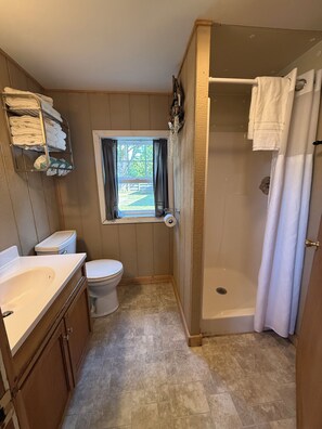 A compact bathroom with a toilet, sink, and shower. - Cabin 3  • 2 BR 1 BA Cabin • Sleeps 5 • Lake Roland Frontage & Trail 3 Access (Toivola)