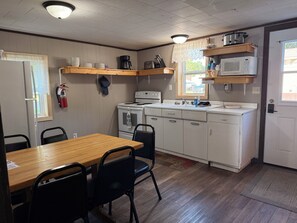 A compact kitchen with white cabinets, a wooden table, and chairs. There are two sinks, a stove, and a microwave. - Cabin 3  • 2 BR 1 BA Cabin • Sleeps 5 • Lake Roland Frontage & Trail 3 Access (Toivola)