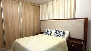 Une chambre à coucher comprenant un lit, une table de chevet, une armoire en bois et un luminaire fixé au plafond.