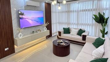 Un salon moderne avec un téléviseur à écran plat, un canapé, une table basse et une grande plante.