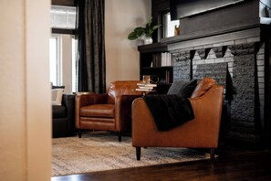 Ein Wohnzimmer mit Kamin, Ledersesseln, einem Couchtisch und einem Bücherregal.