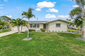 A single-story house with a front lawn, palm trees, and a clear sky. - 
This home away from home is beautifully furnished and located in Cape Coral. (Cape Coral)