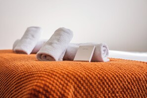 A neatly folded white towel with a tag on a textured orange blanket. - Sutherland Apartments - Apt 36 (London)