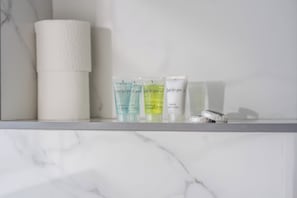 A bathroom shelf with a roll of toilet paper, three toiletry tubes, and a small bottle. - Sutherland Apartments - Apt 36 (London)
