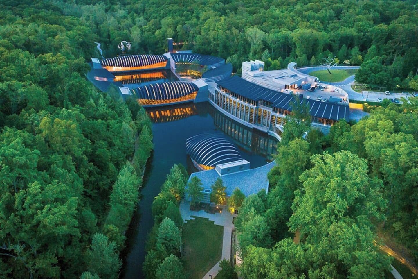 An aerial view of a modern hotel with a central courtyard, surrounded by dense forest.