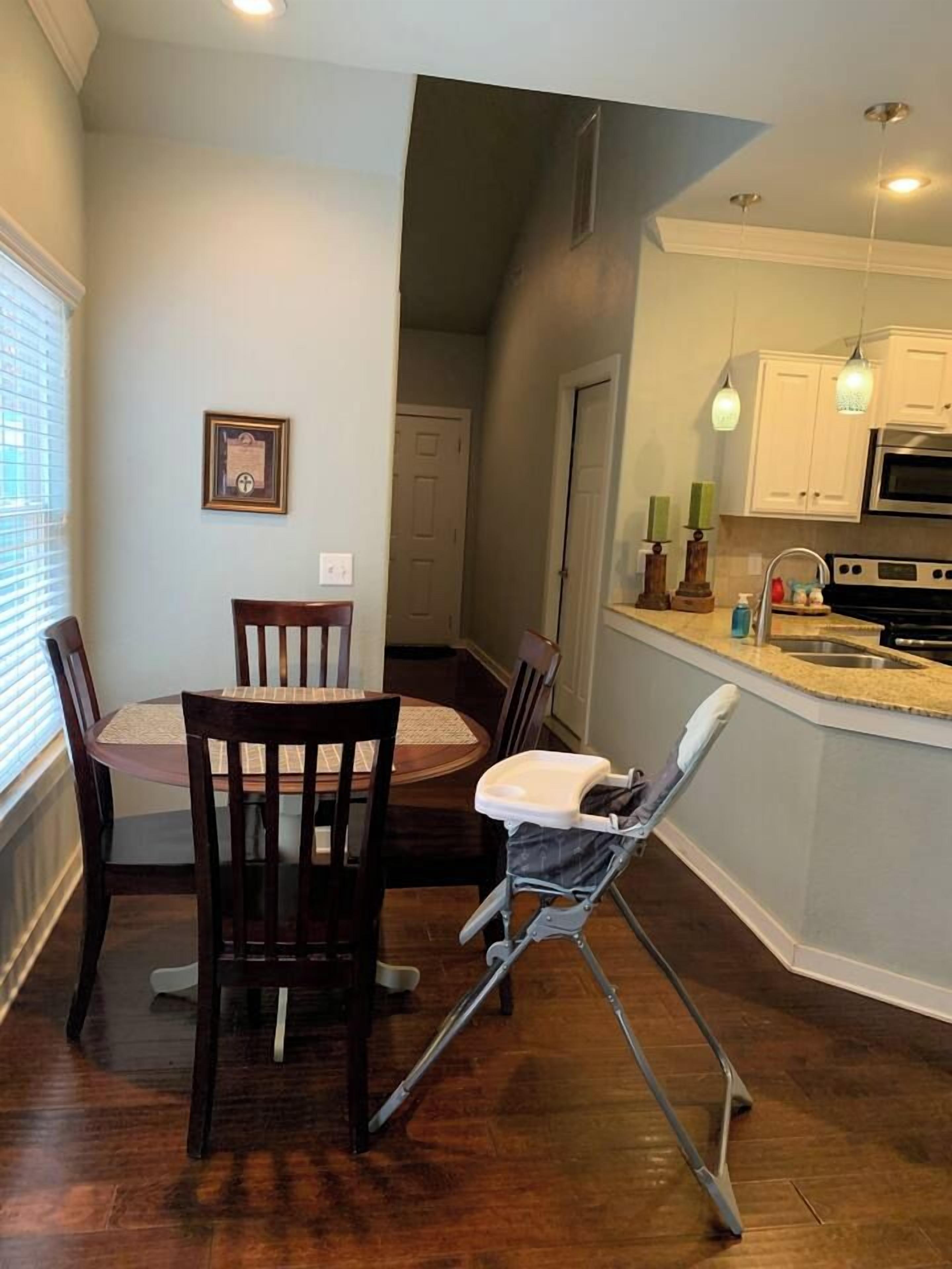 A dining area with a round table and chairs, a baby high chair, and a kitchen with a sink and stove.