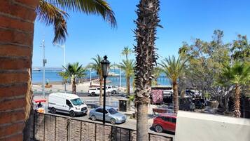A coastal street with parked cars, palm trees, and a view of the sea.